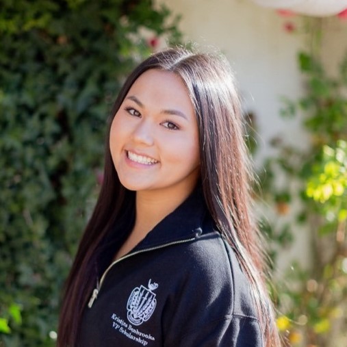 Portrait of a woman with straight, long hair and brown eyes, framed by lush green leaves in the background.